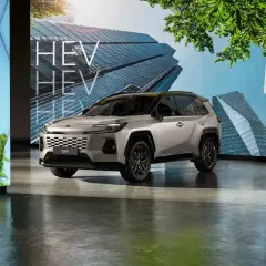 Nowoczesny srebrny Toyota RAV4 HEV prezentowany na tle futurystycznych budynków i zieleni.