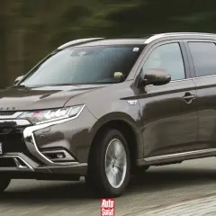 Brązowy Mitsubishi Outlander PHEV w ruchu, z widocznym napisem "OUTLANDER" na masce i emblematem "EV" na błotniku.