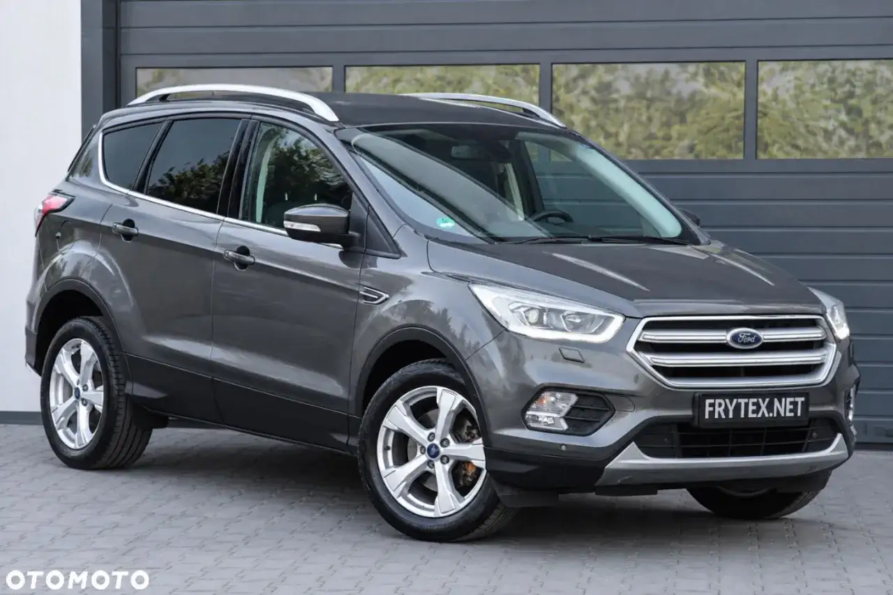 Szary Ford Kuga stoi przed garażem.